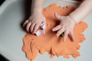 faceless baby is playing with kinetic sand. Child handles with a toy in the shape of a star