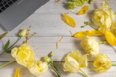 Klasik beyaz ahşap arka planda çiçek deseni ve kısmen bilgisayar. Sarı bahar çiçekleri, serbest kadın konsepti. Yukarıdan görüntüle. 