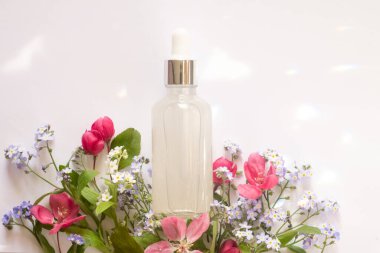 Beyaz arka planda farklı kır çiçekleri arasında hiyalüronik asit için damlatan şeffaf bir şişe. Güzel ışık yansımaları. Üst görünüm ve kopyalama alanı