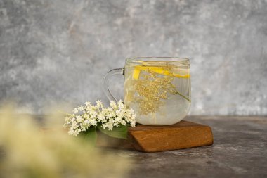 Gri arkaplandaki yaşlı çiçeklerden bir fincan çay. Ahşap bir tahtanın üzerinde yaşlı böğürtlen yaprakları ve enfeksiyonlar. Bulanık ve seçici odaklanma. Bulanık arkaplan. 