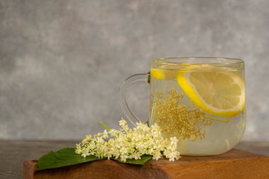 Gri arkaplandaki yaşlı çiçeklerden bir fincan çay. Ahşap bir tahtanın üzerinde yaşlı böğürtlen yaprakları ve enfeksiyonlar. Bulanık ve seçici odaklanma. Tıbbi bitki kavramı