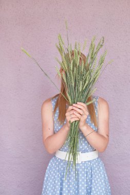 faceless girl with a blue polka dot dress covers her face with a bouquet of dried flowers on a pink background. summer concept. Half-length portrait of a young woman. Copy space 