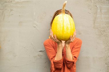  faceless woman holds a big yellow pumpkin in his hands against the background of a cement wall. Copy space. Thanksgiving Day concept 