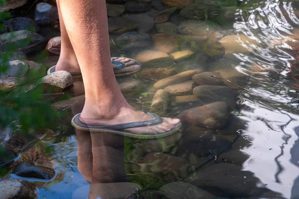 Men feet in slippers stand in a mountain lake on the rocks. Summer hot day