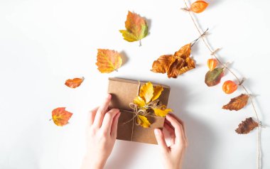 Yüzsüz kadın, beyaz arka planda sonbahar yapraklarıyla bir hediye kutusunu süslüyor. Şükran Günü ve sıfır atık konsepti
