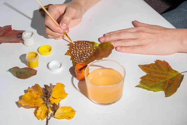 Faceless woman paints autumn leaves with paints on a white background. Creativity and zero waste