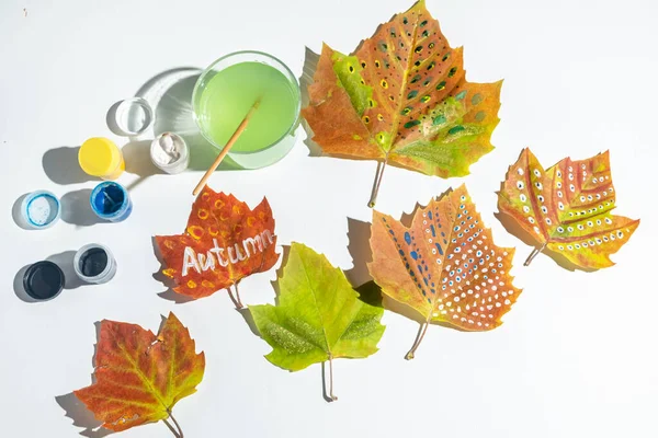 Painted fall leaves on a white background. word Autumn is written on a leaf. Child creativity and zero waste concept