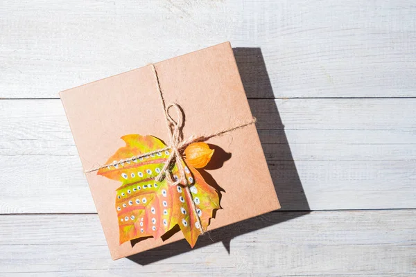 Craft gift box decorated autumn maple leaf on a white board. Thanksgiving and zero waste concept. Copy space