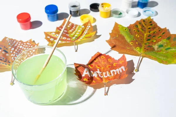 Painted fall leaves on a white background. word Autumn is written on a leaf. Child creativity and zero waste concept