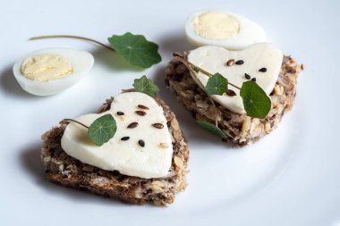 Kalp şeklinde mini tostlar keçi peyniri ve beyaz tabakta bıldırcın yumurtası.