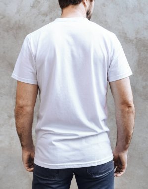 Boş beyaz tişörtlü genç adam. Açık gri beton duvarın arka planında. Yazdırma için erkek tişörtlerinin tasarımı ve düzeni.