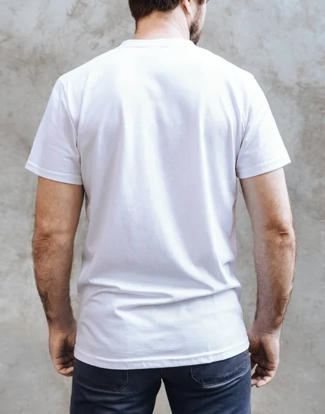 Boş beyaz tişörtlü genç adam. Açık gri beton duvarın arka planında. Yazdırma için erkek tişörtlerinin tasarımı ve düzeni.