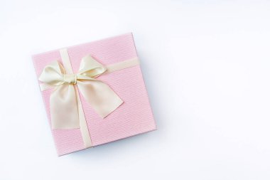 Beyaz arka planda güzel bir fiyonkta saten ışık kurdelesiyle süslenmiş zarif pembe hediye kutusunun üst görüntüsü. Anneler Günü ya da Kadınlar Günü hediyesi. Boşluğu kopyala, düzleştirme biçimi.