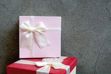 Doğal beton arka planda saten kurdeleli iki güzel hediye kutusunun önü. Yeni yıl ya da Noel için pembe ve kırmızı hediye. Metin için alanı kopyala