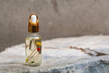 Doğal taş podyum arka planındaki şişenin içinde kurumuş çiçekler ve bitkiler bulunan cam damlacıklar için yumuşak bir odak noktası. Eko-krem, serum, kozmetik ürünleri, masaj yağı. Ön görünüm, Boşluğu Kopyala