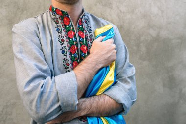 Yumuşak Seçici Odak Adam, Ukrayna 'nın mavi ve sarı ulusal bayrağını kalbinde taşıyor. Arka planda desenli beton bir duvarda geleneksel işlemeli gömlekli bir adam. Boşluğu kopyala