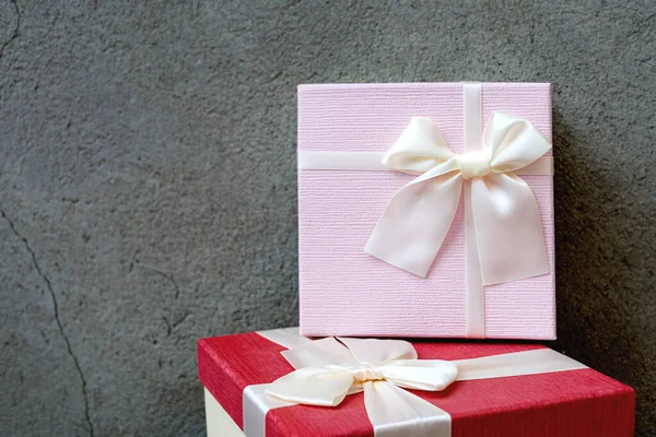 Doğal beton duvarın arka planında saten kurdele olan iki güzel hediye kutusunun önü. Babalar Günü ya da Noel için pembe ve kırmızı hediye. Metin için alanı kopyala