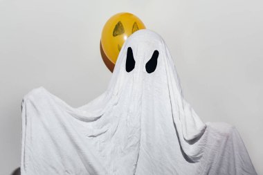 Mutlu Cadılar Bayramı. Beyaz ev yapımı hayalet kostümü giyen ve turuncu topları boyayan bir çocuk. Şenlik tasarımı, parti konsepti. Azizler Günü kutlaması.