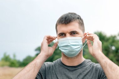 Yeşil Park 'ta salgın, aşı, hastalık ya da karantina nedeniyle mavi maskeli yakışıklı bir adamın portresi. Koronavirüs kavramının sosyal uzaklık süresince yaşam tarzı