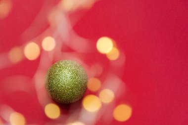 Defocused focus on green round christmas decoration on red background under yellow bright twinkling bokeh. The view is straight. Copy space for text.