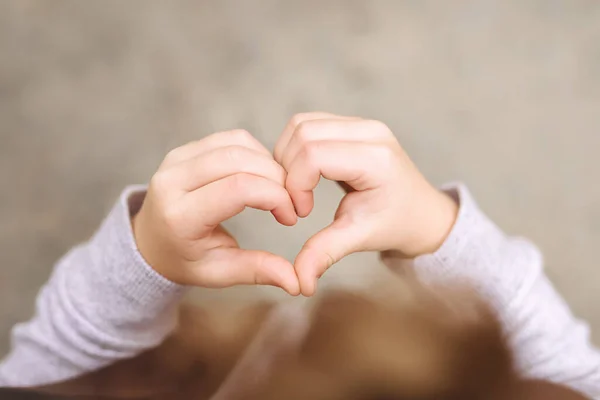 Close-up of a heart from the hands of a child making a shape with his hands on a gray background. A sign of love and happiness. Soft Selective focus