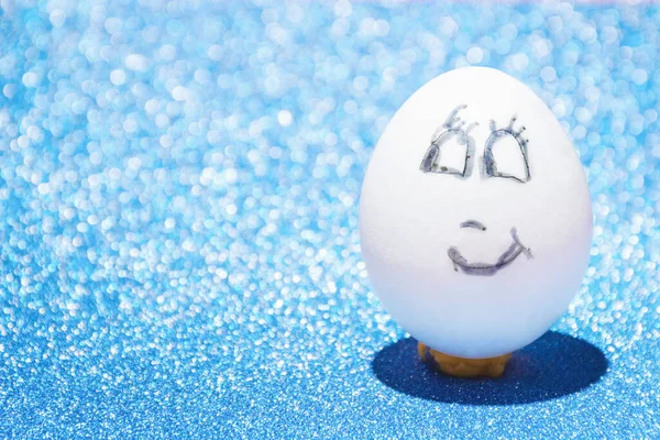 Beyaz Paskalya yumurtası mavi parlak bir arka planda gülümseyen neşeli yüzlü. Tatil ve nakış işi kavramı.
