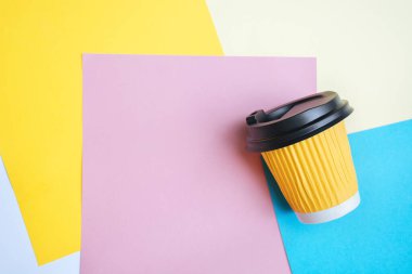 Sarı kahve fincanına yumuşak seçici odak tasarım masasındaki renkli kağıtta yaratıcı bir karmaşada yatar. Mavi, turuncu ve pembe arka plan. Metin için alanı kopyala