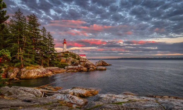 Lighthouse Park on a rocky coast during a dramatic cloudy sunset. — Stock Photo, Image