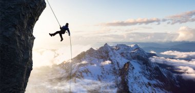 Yetişkin maceraperest bir adam kayalık bir uçurumdan iple iniyor..