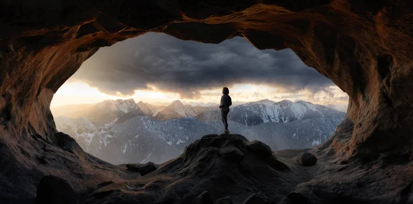 Eine erwachsene Wanderin steht in einer Felshöhle. Dramatischer bunter Sonnenuntergang — Stockfoto