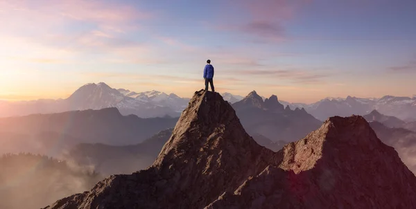 Kalandos ember túrázó áll a tetején egy sziklás hegy, kilátással a drámai táj — Stock Fotó