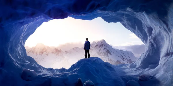 岩の多い山を背景に氷の洞窟に立つ冒険的な男のハイカー. — ストック写真