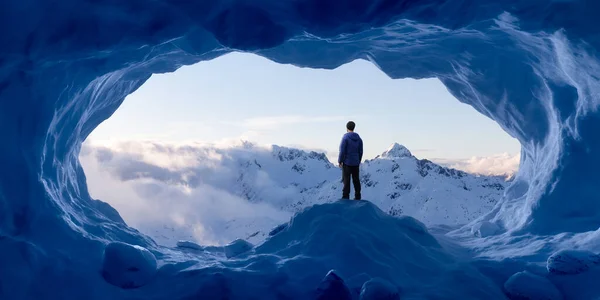 Uomo avventuroso Escursionista in piedi in una grotta di ghiaccio con montagne rocciose sullo sfondo — Foto Stock