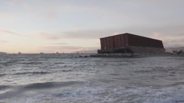 Mavna konteyneri fırtınada kayalık bir kıyıda çarpışmış. Günbatımı Gökyüzü.