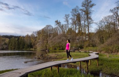 Kıyı şeridinde yeşil ağaçlarla Tahta Yol 'da Yürüyen Kadın