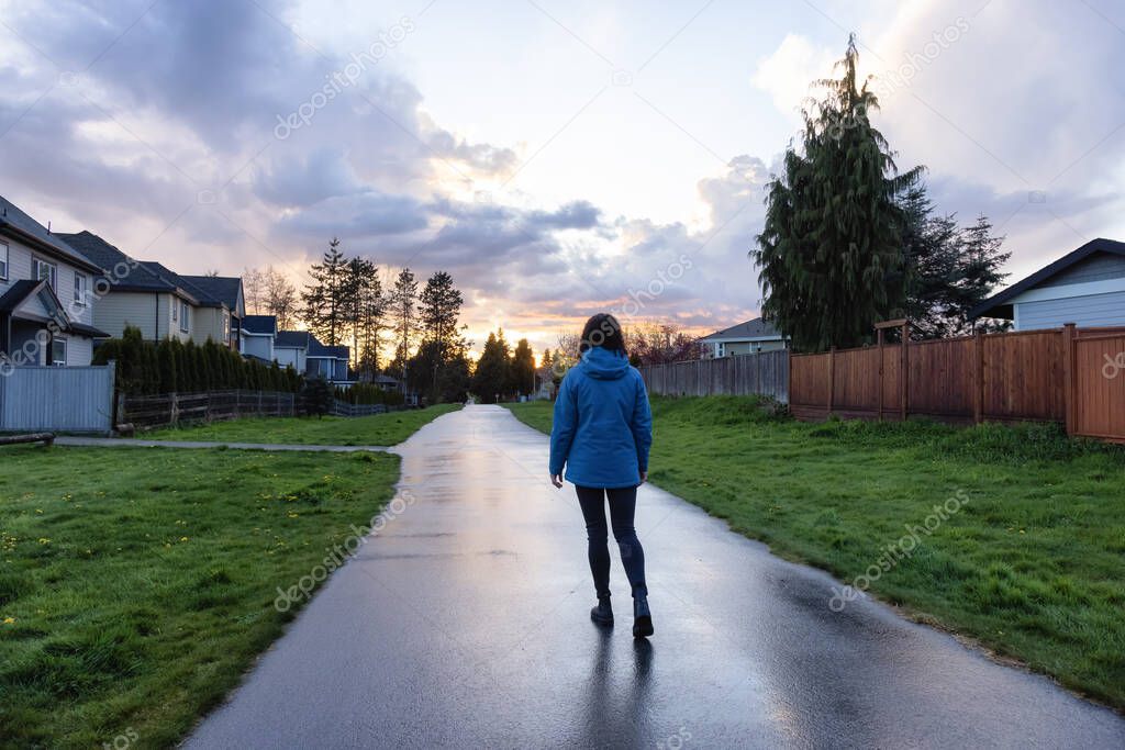 Woman walking on a path in a residential neighborhood of modern city suburbs.
