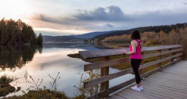 Kıyı şeridinde yeşil ağaçlarla Tahta Yol 'da Yürüyen Kadın