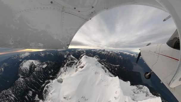 Pesawat kecil bermesin tunggal terbang di atas lanskap pegunungan berbatu tertutup salju. — Stok Video
