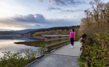 Kıyı şeridinde yeşil ağaçlarla Tahta Yol 'da Yürüyen Kadın