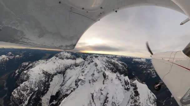 Pequeño avión de un solo motor volando sobre el paisaje de montaña rocosa cubierto de nieve. — Vídeo de stock