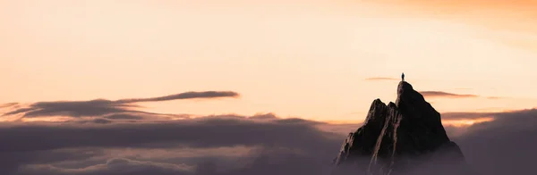 Homem Adventuroso Caminhante em pé no topo de uma montanha rochosa com vista para a paisagem dramática ao pôr do sol. — Fotografia de Stock
