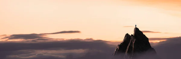 Hombre aventurero excursionista De pie en la cima de una montaña rocosa con vistas al paisaje dramático al atardecer. —  Fotos de Stock