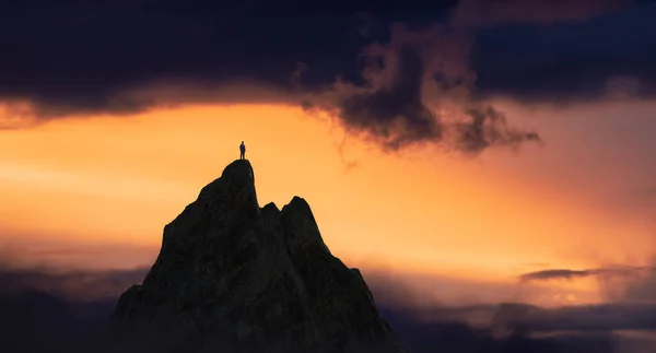Kalandos ember túrázó áll a tetején egy sziklás hegy kilátással a drámai táj naplementekor. — Stock Fotó