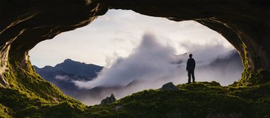 Kayalık bir mağarada duran maceraperest adam. Arka planda bulutlar olan Dağ Doğası manzarası. Sunny Sunrise veya Sunset. 3d Macera Hazırlama Sanatı.