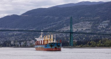 Vancouver, British Columbia, Kanada - 7 Mayıs 2022: Aslanlar Kapısı Köprüsü ve dağlarla Vancouver Limanı 'na gelen kargo gemisi.