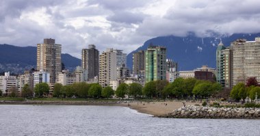 Stanley Park yakınlarındaki konutlar ve Vancouver 'daki English Bay Sahili, British Columbia, Kanada. Pasifik Okyanusu 'nun batı kıyısı ve arka planda dağlar.