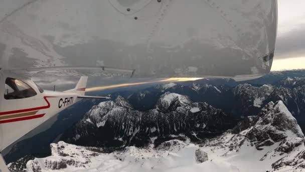 バンクーバー ブリティッシュコロンビア州 カナダ 2022年2月 雪の上を飛ぶ小型シングルエンジン飛行機は岩だらけの山の風景を覆いました 曇った冬の夜 広角魚眼レンズ — ストック動画