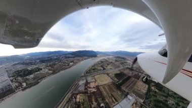 Small Single Engine Airplane flying over Pitt Meadows. Cloudy winter evening. Wide Angle Fish Eye Lens. Greater Vancouver, British Columbia, Canada.