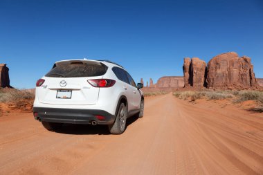 Oljato-Monument Valley, Utah, United States - June 6, 2022: Mazda CX-5 Riding on a Scenic Road in the Dry Desert with Red Rocky Mountains in Background.