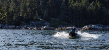 Adventurous Caucasian Woman on Jet Ski riding in the Ocean. Lighthouse park in background. West Vancouver, British Columbia, Canada.